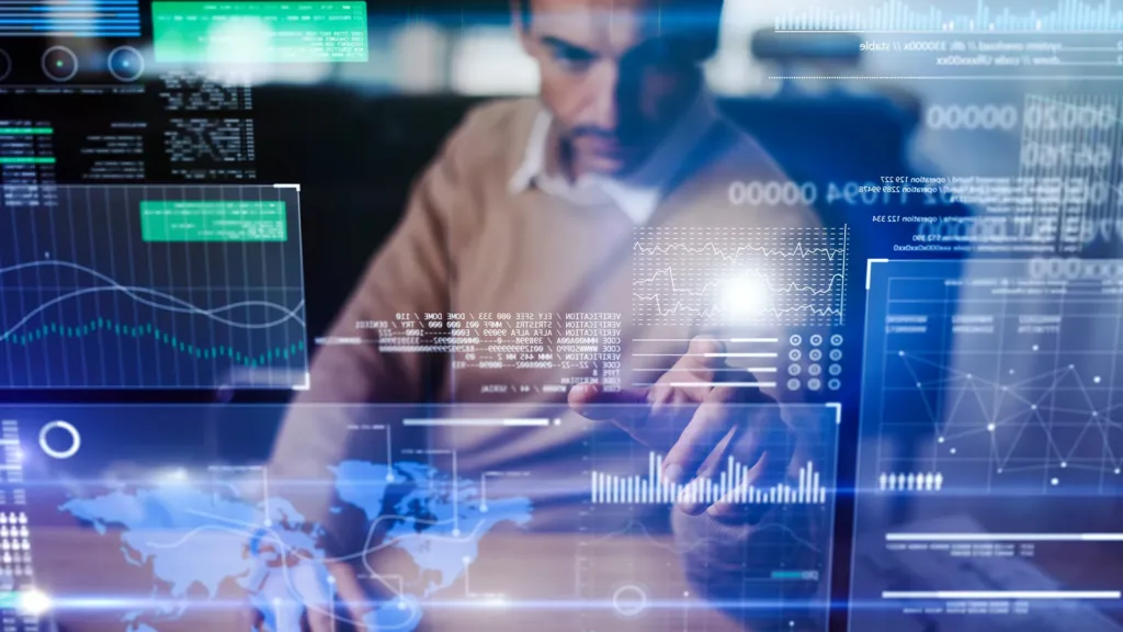A person interacts with glowing data visualizations, graphs, and world maps on a transparent screen. The scene conveys a futuristic and analytical atmosphere.